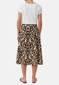 Haut blanc à manches courtes avec une bordure noire, associé à une longue jupe à motifs présentant un design abstrait dans des teintes de marron et de crème.