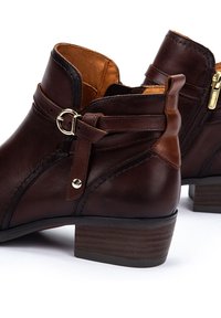 Stivali alla caviglia in pelle marrone con zip laterale, fibbia decorativa e tacco impilato. L'interno è foderato in pelle marrone chiaro.