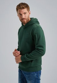 Green hooded sweatshirt with a front pocket, ribbed cuffs, and a small emblem on the chest. Smooth texture and casual fit.