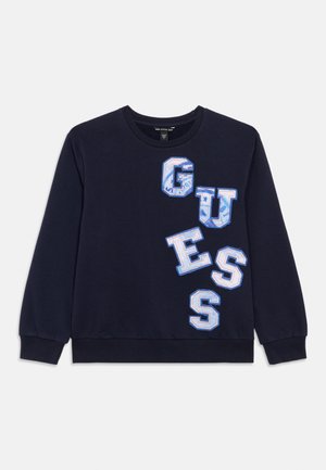 Felpa blu navy con scollo girocollo a coste. Presenta grandi lettere "GUESS" ricamate in bianco e azzurro con un motivo testurizzato.