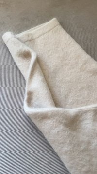 Villa viltti pehmeässä beige-sävyssä, jossa on hieman karhea pinta ja taitetut reunat, lepää raitaisella harmaalla taustalla.