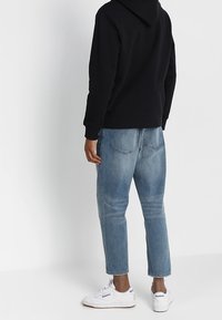 Felpa nera con cappuccio, jeans in denim azzurro chiaro, sneakers bianche. I jeans hanno una vestibilità comoda con orli ripiegati e tasche posteriori.