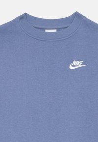 Zila kreklveida jaka, kas izgatavota no mīksta auduma, ir ar ribotu apkakli un baltu Nike logo augšējā kreisajā stūrī.