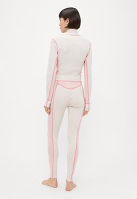 Σετ αθλητικής ένδυσης από φλις σε ανοιχτό ροζ χρώμα με ανάγλυφο λουλουδάτο σχέδιο, διαθέτει ραφές σε αντίθεση ροζ και μπουφάν με ψηλό γιακά.