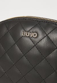 Bolso negro de piel sintética acolchada con una cremallera dorada y el logotipo grabado "LIU·JO". Presenta una superficie texturizada y un diseño de costura en forma de diamante.