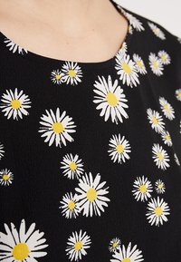 Svart tyg med ett prästkragormönster som har vita blad och gula mittar; slät textur och rundad nackdesign.