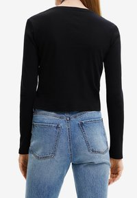 Schwarzes, geripptes Langarmoberteil mit einem cropped Design und rundem Halsauschnitt. Kombiniert mit hochgeschnittenen blauen Jeans mit Taschen.