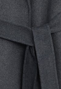 Ceinture de manteau en laine grise nouée en un nœud lâche autour de la taille sur un fond de tissu texturé.