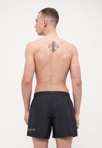 Sorts de baie negri cu talie elastică, având un logo aurii "Armani" pe piciorul stâng și o textură fină, ușoară.