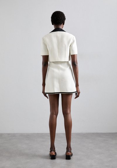 Weißes, strukturiertes Kleid mit kurzen Ärmeln und schwarzem Kragen, das eine taillierte Form hat und einen kontrastierenden schwarzen Saum aufweist.