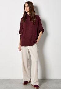 Top de punto gris burdeos de gran tamaño con cuello estilo cowl, combinado con pantalones de pierna ancha en color crema y zapatos de deslizamiento burdeos. Textura suave, ajuste holgado.