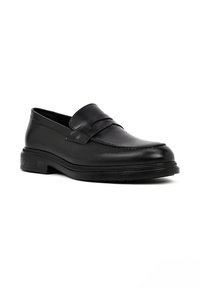 Mocasin de piel negra con punta redondeada, banda decorativa cruzando el empeine y suela de goma texturizada. Acabado suave y diseño elegante.