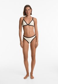 Set da bikini in crema con accenti neri; top triangolo con spalline sottili e slip a vita alta coordinati che presentano un simile gioco di colori.