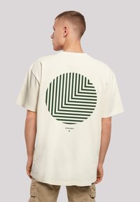Cream-colored t-shirt featuring a large circular graphic on the back, with green diagonal stripes and a small text detail at the bottom.