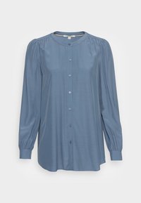 Blouse à manches longues bleu clair avec un col rond, une fermeture à boutons sur le devant et des épaules froncées. Tissu lisse avec une coupe légèrement ample.