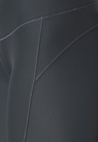 Leggings neri a vita alta realizzati in tessuto elastico con cuciture grigie a contrasto e una texture liscia, caratterizzati da un design a cucitura triangolare.