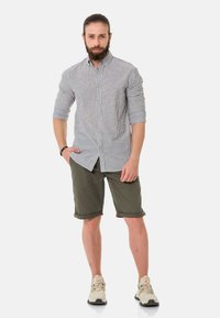 Gestreepte overhemden in blauw- en wittonen, gecombineerd met olijfgroene shorts. Sneakers met een crèmekleurige accent maken de outfit compleet.