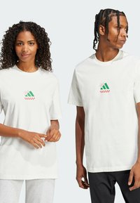Witte katoenen t-shirts met korte mouwen, met een kleurrafische afbeelding van groene strepen en een rood ruitpatroon op de borst.
