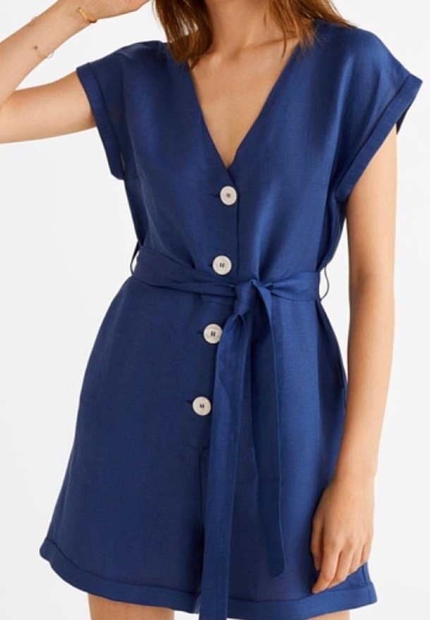 Femme portant une robe bleu marine à manches courtes avec quatre boutons blancs sur le devant et une ceinture assortie en tissu nouée à la taille.