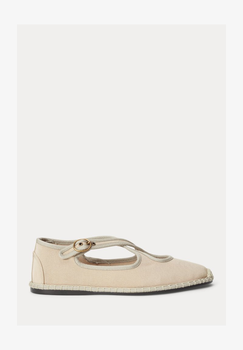 Μπεζ υφασμάτινο φλατ παπούτσι με στρογγυλεμένη μύτη, λουράκι στον αστράγαλο, ορειχάλκινη αγκράφα και μαύρη σόλα με ραμμένη λεπτομέρεια περιμετρικά.