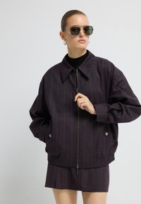 Donkerpaars gestreepte jas met een rits aan de voorkant en een grote kraag, voorzien van zilverkleurige hardware en elastische manchetten, gecombineerd met een geplooide rok.