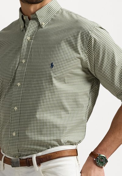 Πράσινο και λευκό καρό πουκάμισο με κουμπωτό γιακά, διακοσμημένο με μπλε έμβλημα. Συνδυασμένο με καφέ ζώνη και ασημένιο ρολόι.