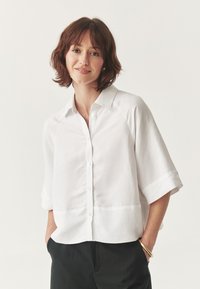 Camicia bianca con colletto aperto, realizzata in tessuto leggero, con maniche corte e una vestibilità rilassata. Design minimalista senza motivi.