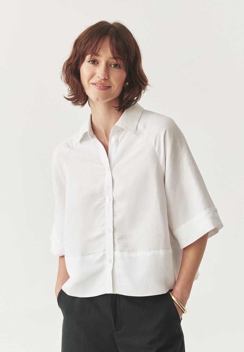 Camicia bianca con colletto aperto, realizzata in tessuto leggero, con maniche corte e una vestibilità rilassata. Design minimalista senza motivi.