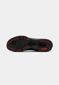 Semelle de chaussure de sport noire avec un motif de grip texturé, des accents rouges et un design épuré avec une rainure centrale de flexion.