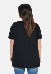 Camiseta de algodón negra con un corte holgado, escote redondo y mangas cortas, que llega hasta las caderas, combinada con jeans azules.