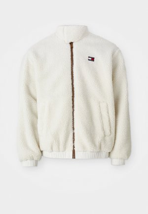 Veste en polaire couleur crème avec col montant, deux poches latérales, une fermeture éclair frontale marron et des poignets et un ourlet élastiques. Patch logo sur la poitrine.
