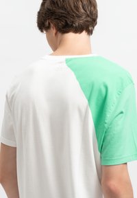 T-shirt met korte mouwen, bestaande uit een witte basis met een groene schouderpaneel aan de linkerkant, gemaakt van zachte katoen met een relaxte pasvorm.