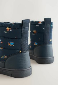 Mørkeblå støvler med quiltet design, der har farverige mønstre med byggeplads køretøjer. Gummisåler og stoftrækstropper bagpå.