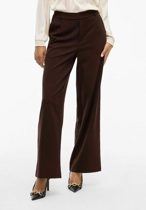 Bruine wijde broek gemaakt van een gladde stof, met riemlussen, voorplooien en gecombineerd met zwart puntige hakken met gouden accenten.