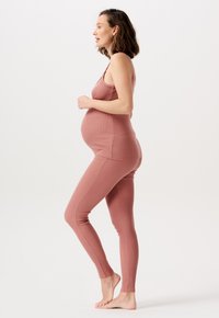 Schwangerschaftsoutfit in einem sanften Rosaton, bestehend aus einem figurbetonten Tanktop mit dünnen Trägern und dehnbaren Leggings, die für Komfort und Unterstützung sorgen.