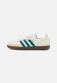 White leather sneaker with green stripes, round toe, textured rubber sole, and embossed logo. Classic design with contrasting accents.