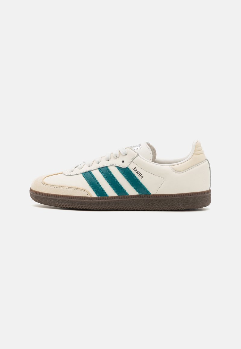 White leather sneaker with green stripes, round toe, textured rubber sole, and embossed logo. Classic design with contrasting accents.