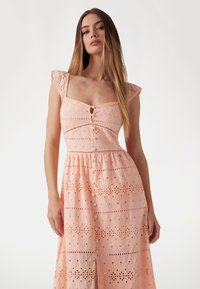 Peach-colored dress with eyelet fabric, short flutter sleeves, square neckline, front buttons, and a flowing skirt with cut-out patterns.