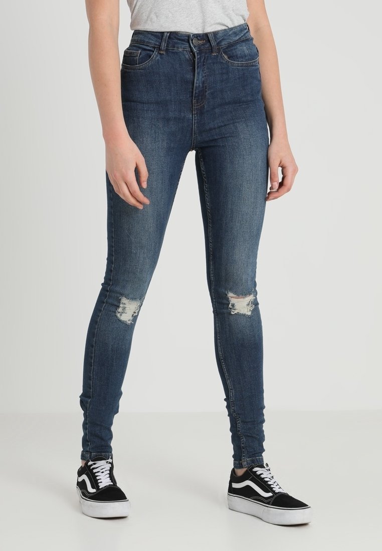 Höga denimjeans i mörkblått med slitna knäpartier. Matchas med svartvita sneakers med klassisk design.