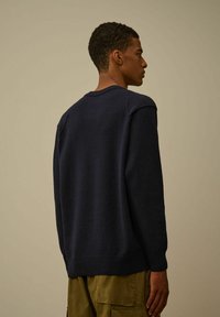 Maglione blu navy realizzato in tessuto a maglia strutturata, con scollatura a girocollo e polsini e orlo a coste, mostrato da dietro.