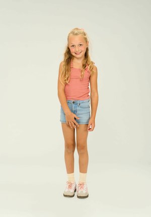Rosa ribbad linne med volangband, denimshorts och rosa sneakers. Bakgrunden är helt vit, vilket tydligt visar upp outfiten.