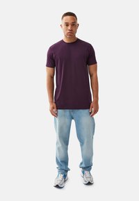 Lilla bomulds T-shirt med korte ærmer. Kombineret med lyseblå jeans og grå træningssko med blå accenter. Enkelt, casual design.