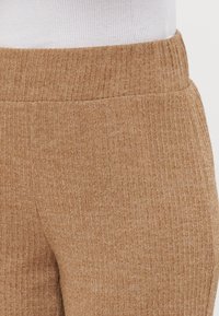 Ribbed, camel-colored fabric featuring a soft texture with an elastic waistband. Close-up view highlights material and pattern details.