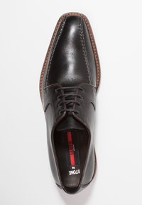 Chaussure habillée en cuir noir avec un bout pointu, un design à lacets, des coutures marron contrastantes et une texture lisse. Intérieur avec une étiquette rouge et noire.