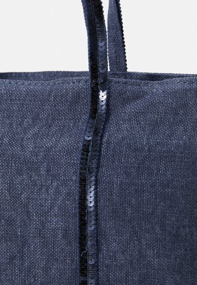 Sac fourre-tout en tissu bleu présentant une texture lisse, orné d'une ligne verticale de paillettes noires brillantes au centre. Les poignées sont en bon état.