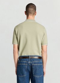 Polo manches courtes vert clair avec un motif texturé et une bordure de col blanche, associé à un jean bleu foncé et une ceinture marron.