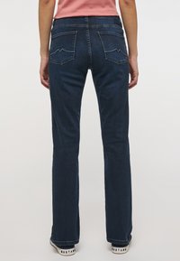 Jean bleu foncé avec une coupe slim bootcut, présentant des coutures discrètes aux poches arrière et une texture en denim lisse.
