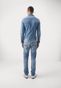 Jeansjacka och jeans i ljusblått, med en figurnära design, klassisk sömnad och diskreta detaljer på bakfickorna. Texturerad yta synlig.