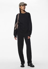 Svart oversize sweatshirt och matchande byxor, kombinerade med en leopardmönstrad keps och rem, med en mjuk textur och avslappnad passform.