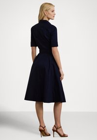 Tmavomodré šaty s priliehavým živôtikom, krátkymi rukávmi a plisovanou sukňou. Majú golierový výstrih a zvýraznený pás.